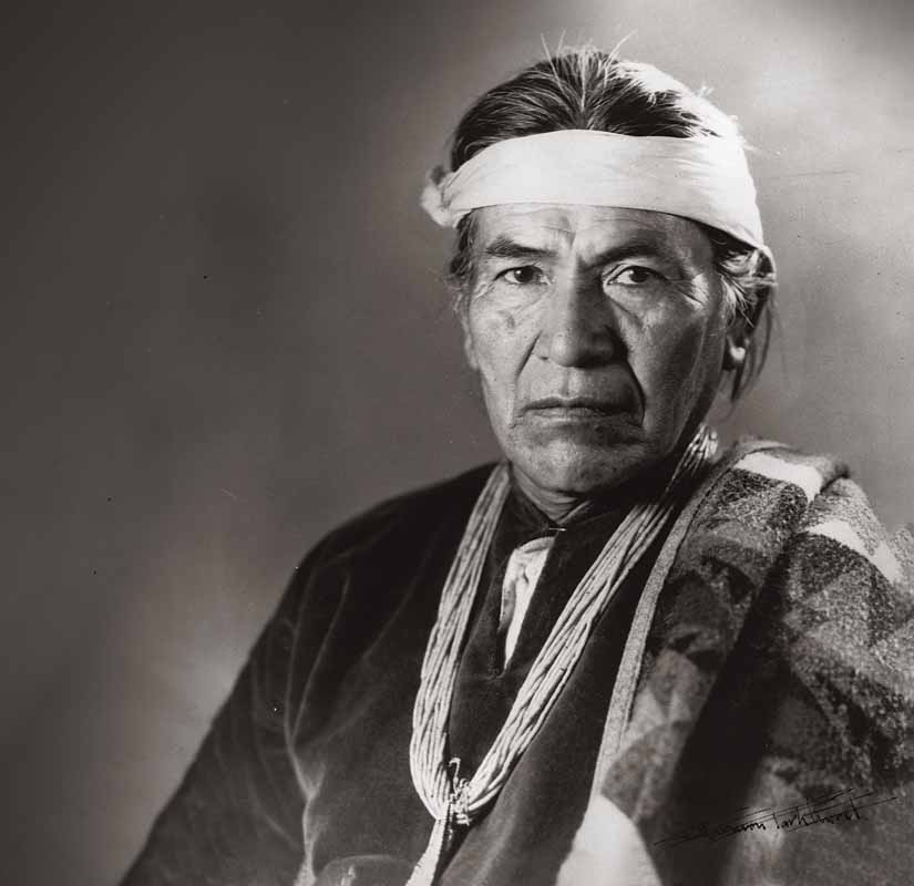 Portrait of Hosteen Klah, circa 1920. This is a studio-style portrait taken by T. Harmon Parkhurst, a photographer who worked extensively in New Mexico. Klah is pictured wearing a traditional headband and Navajo jewelry. 